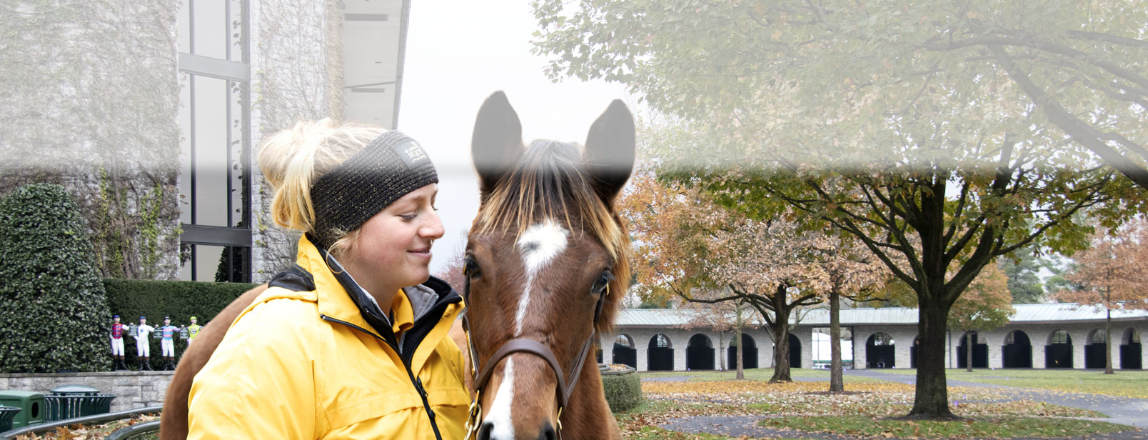 A woman smiles while standing next to a brown horse wearing a halter.